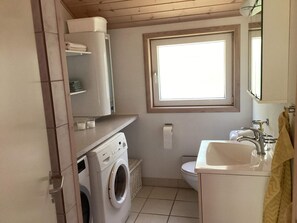 A compact bathroom with a washing machine, toilet, sink, and a window providing natural light.
