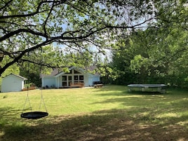 A backyard with a swing, a trampoline, a shed, and a house with a large window.
