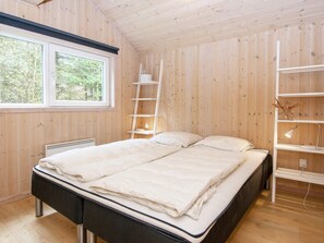 A wooden-paneled bedroom with a bed, a window, a radiator, and a shelf with a lamp. - 6 Person Holiday Home in Oksbol (Oksbol)