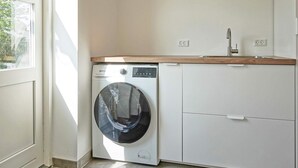 A laundry room with a front-loading washing machine, a sink, and a cabinet.