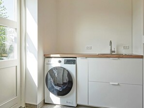 A laundry room with a front-loading washing machine, a sink, and a cabinet.