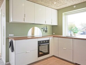 A kitchen with white cabinets, a wooden countertop, a built-in oven, and a window with a view of the outside.