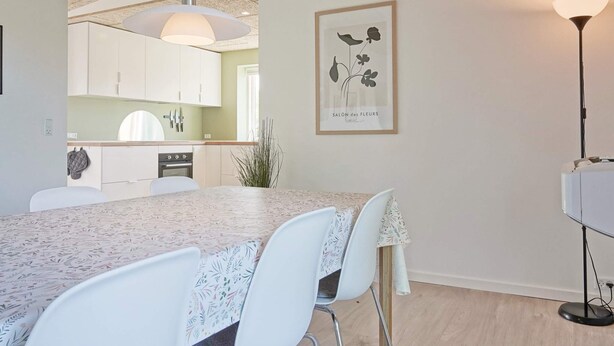 A dining area with a table, chairs, a pendant light, and a framed botanical print on the wall.