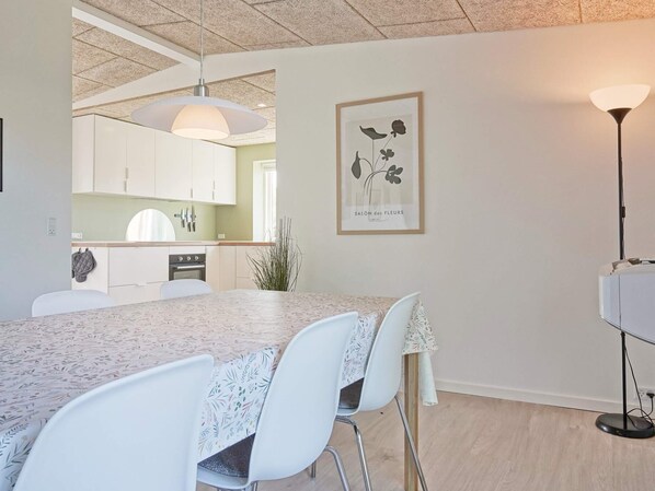 A dining area with a table, chairs, a pendant light, and a framed botanical print on the wall.