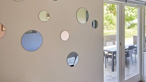 Una habitación con varios espejos redondos en la pared, y un ventanal de vidrio que da a un patio exterior con una mesa y sillas.