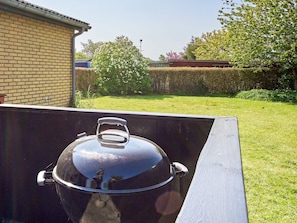Una barbacoa amb tapa, situada a l'exterior davant d'una paret de maó i un jardí amb gespa.