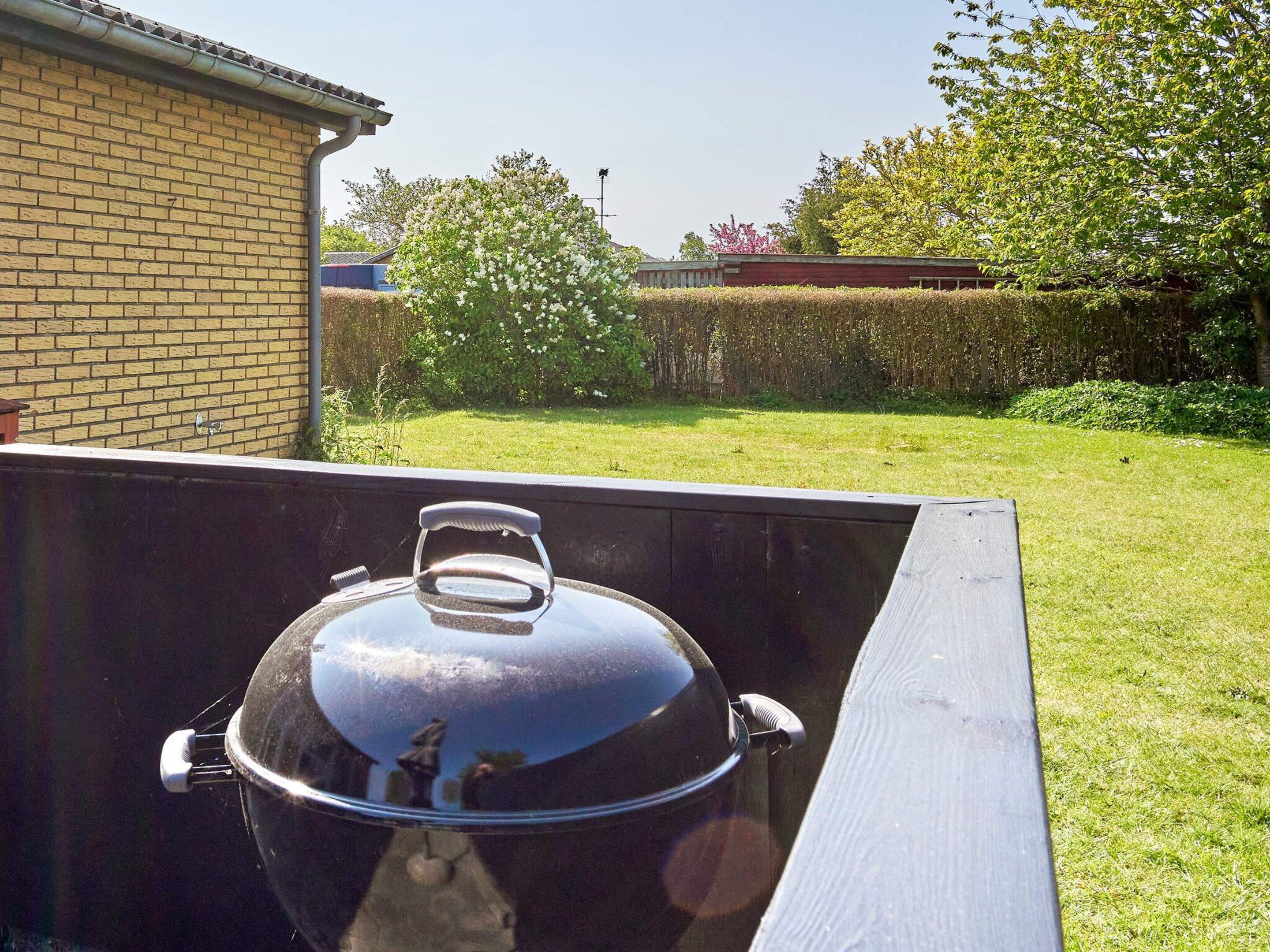 A barbecue grill with a lid, positioned outdoors with a brick wall and a grassy yard in the background.