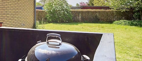A barbecue grill with a lid, positioned outdoors with a brick wall and a grassy yard in the background.