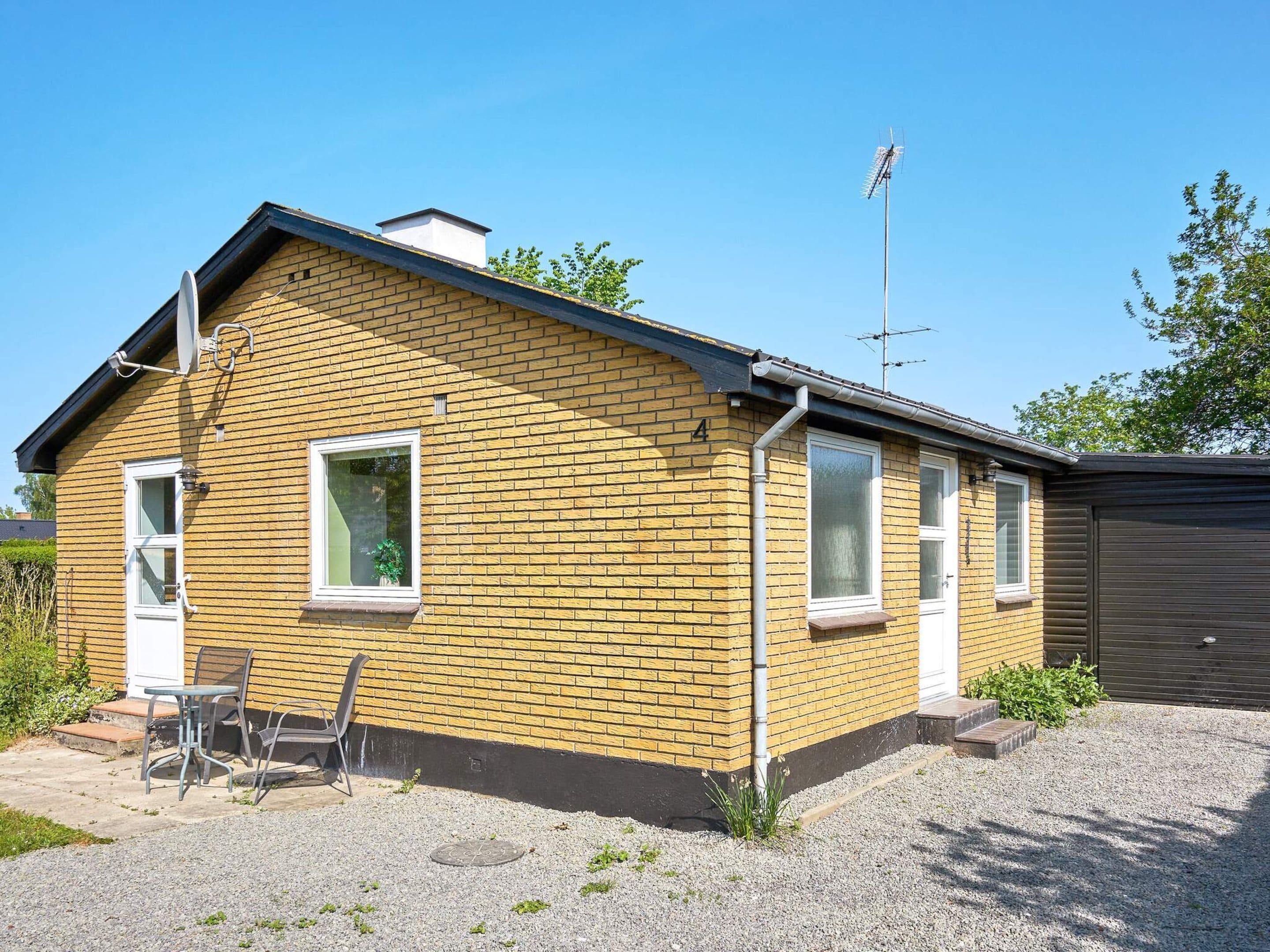 Une maison de plain-pied en briques, avec un garage, une antenne parabolique et une petite terrasse dotée d’une table et de chaises.