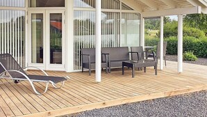 A covered outdoor area with a wooden deck, seating, and a glass door leading to an interior space. - 6 Person Holiday Home in Vaeggerlose (Vaeggerlose)