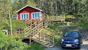Une cabane rouge avec un escalier en bois menant à une terrasse, le tout entouré de forêt.