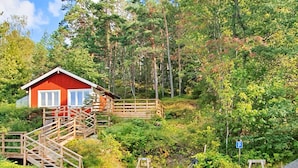 Une cabane rouge avec un escalier en bois menant à une terrasse, le tout entouré d’une forêt dense.