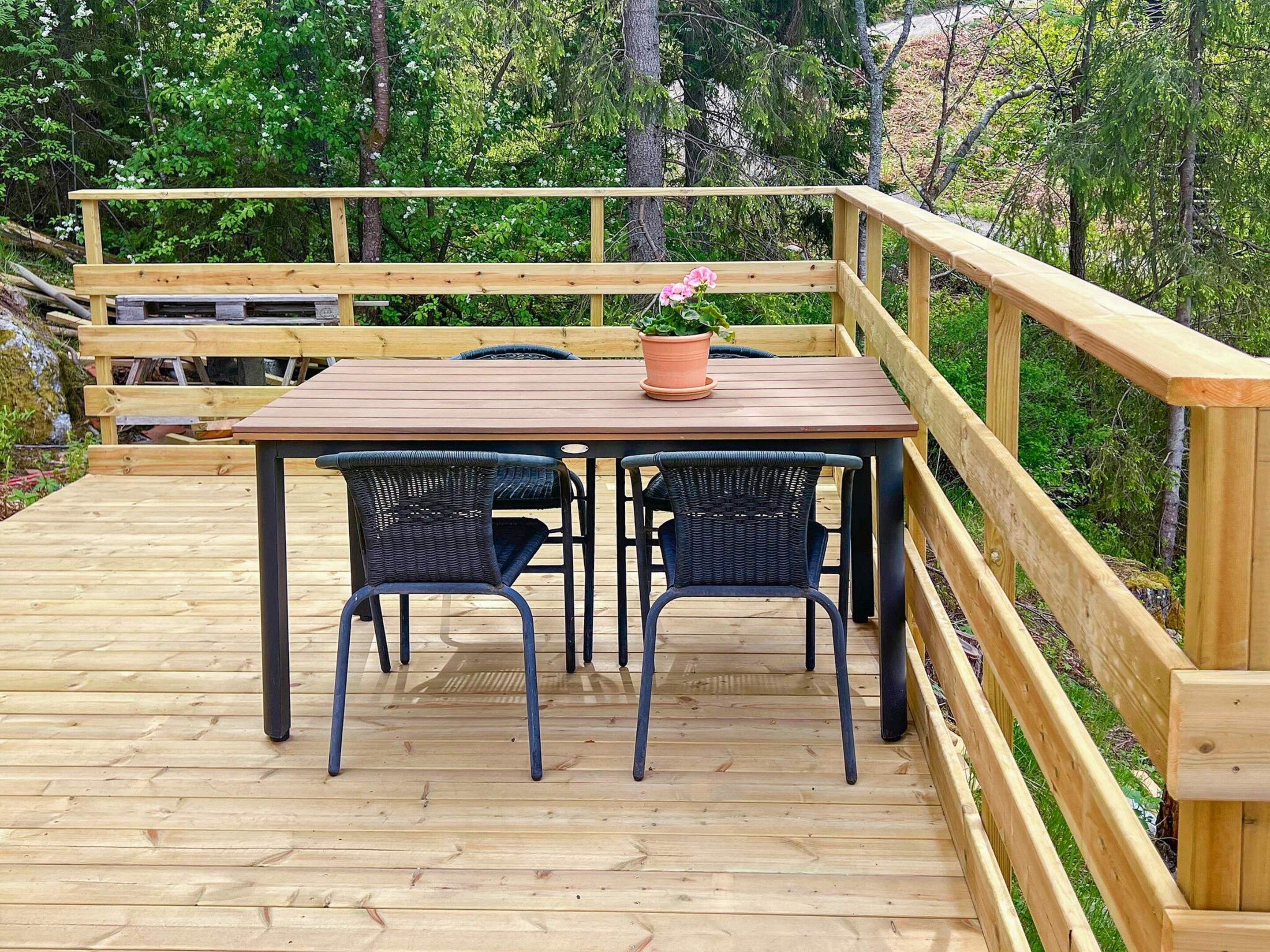 A wooden deck with a table and chairs, surrounded by a wooden railing and trees.