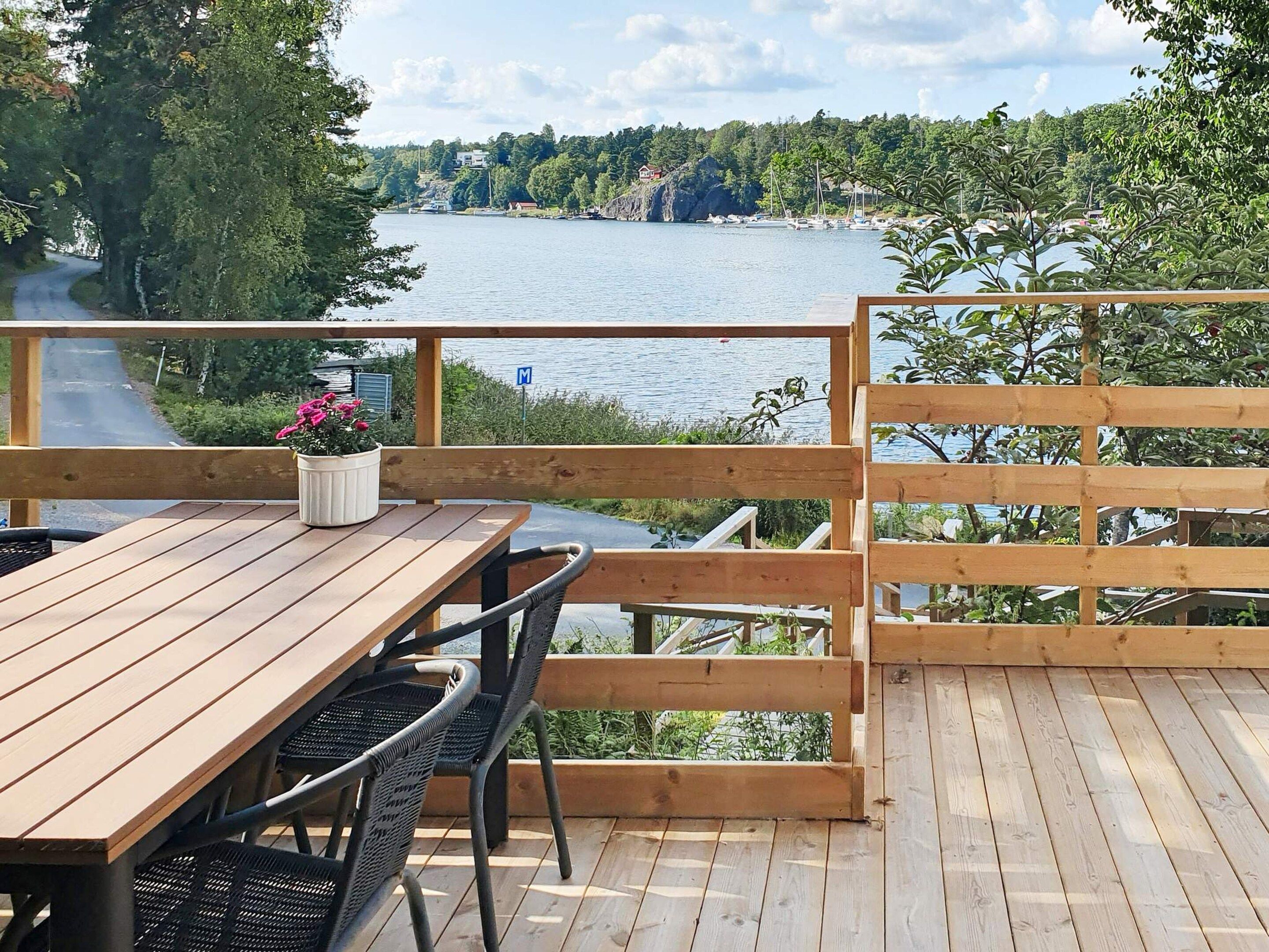 A wooden deck with a table and chairs, overlooking a lake with boats and a forested hillside.