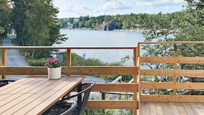 Une terrasse en bois avec une table et des chaises, donnant sur une étendue d’eau et une zone boisée.
