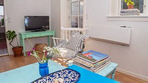 A cozy living room with a television, a bookshelf, a window with a plant, and a blue table with decorative items. - 6 Person Holiday Home in Lemvig (Lemvig)