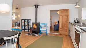 A cozy living room with a wood-burning stove, a dining area with a table and chairs, and a kitchen with a stove and sink. - 6 Person Holiday Home in Lemvig (Lemvig)