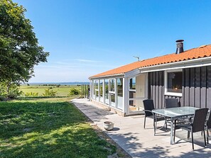 A house with a glass enclosure patio, a table with chairs, and a view of the landscape. - 7 Person Holiday Home in Hojslev (Hojslev)