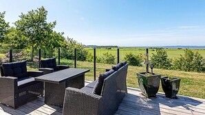 An outdoor deck with wicker furniture and planters, overlooking a grassy field and distant horizon.