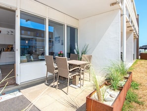 A patio with wicker furniture, a glass door leading to a kitchen, and a view of a building across the street.