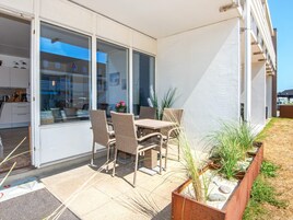 Un patio con mobiliario de mimbre, una puerta de cristal que da a una cocina y vista a un edificio de la calle.