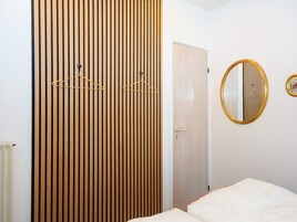 A room with a bed, a wooden slat partition, a door, and a round mirror on the wall.