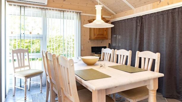 A dining area with a white table and chairs, a hanging light fixture, and a view of the outdoors through a window. - 6 Person Holiday Home in Vaeggerlose (Vaeggerlose)