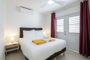 A hotel room with a bed, bedside table, lamp, air conditioning unit, and a window with curtains.