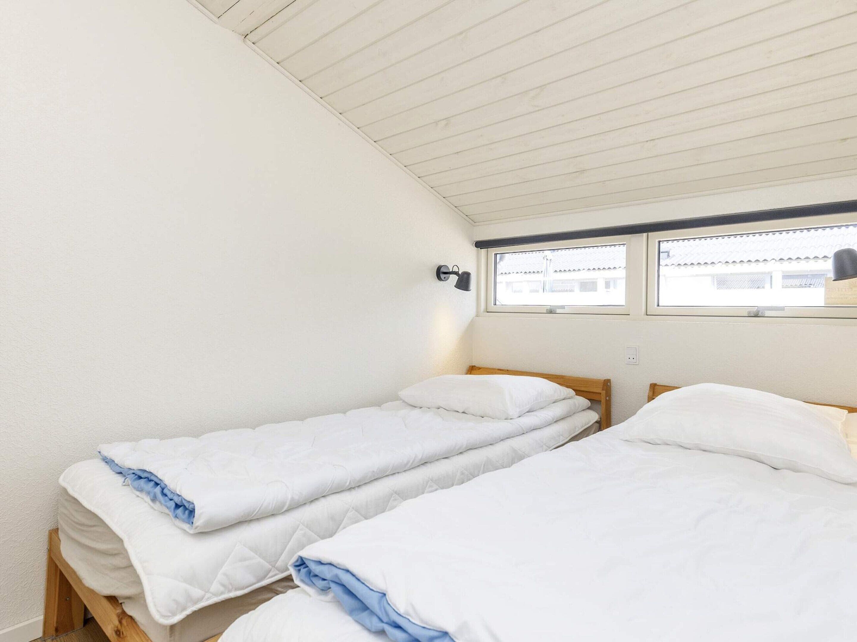 A room with two single beds, a window with a view, and a wall-mounted lamp.