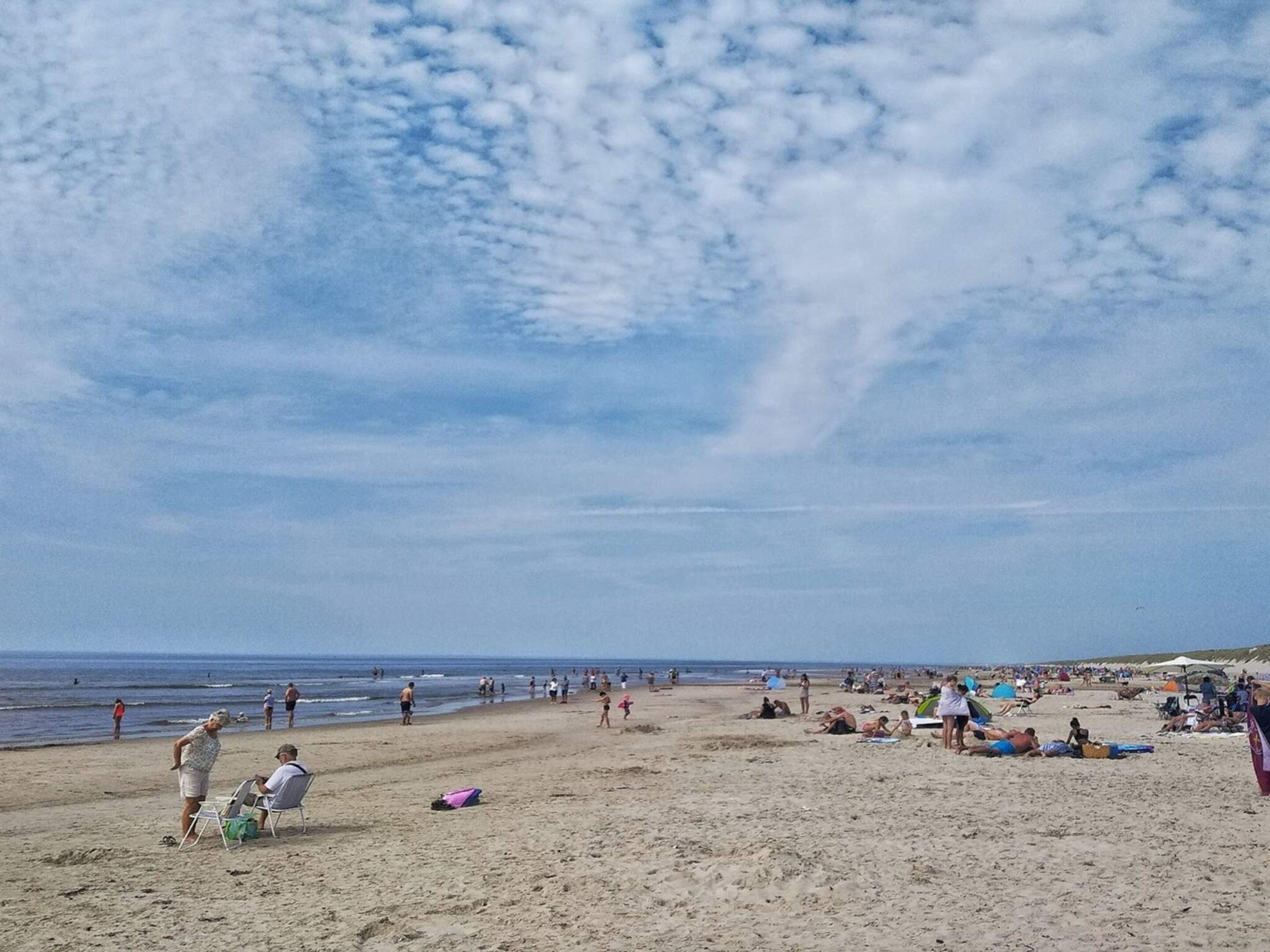 Een strand met mensen, sommigen zitten en anderen staan, en een heldere lucht.