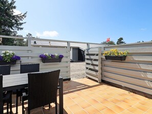 An outdoor patio area with a table and chairs, wooden slatted walls, and flower planters. - 2 Person Holiday Home in Vejers Strand (Vejers Strand)
