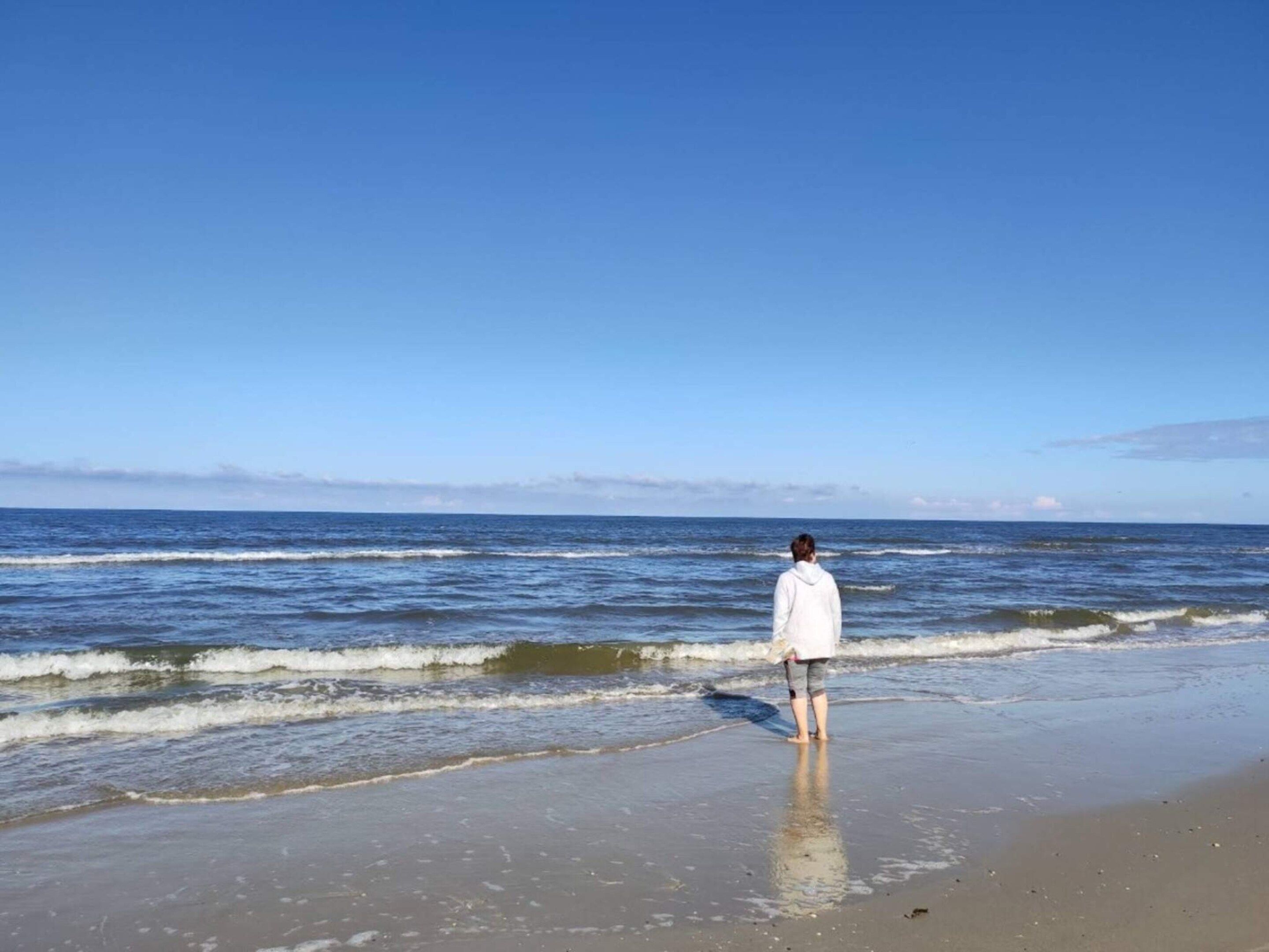 Une personne se tient sur une plage, face à l’océan.