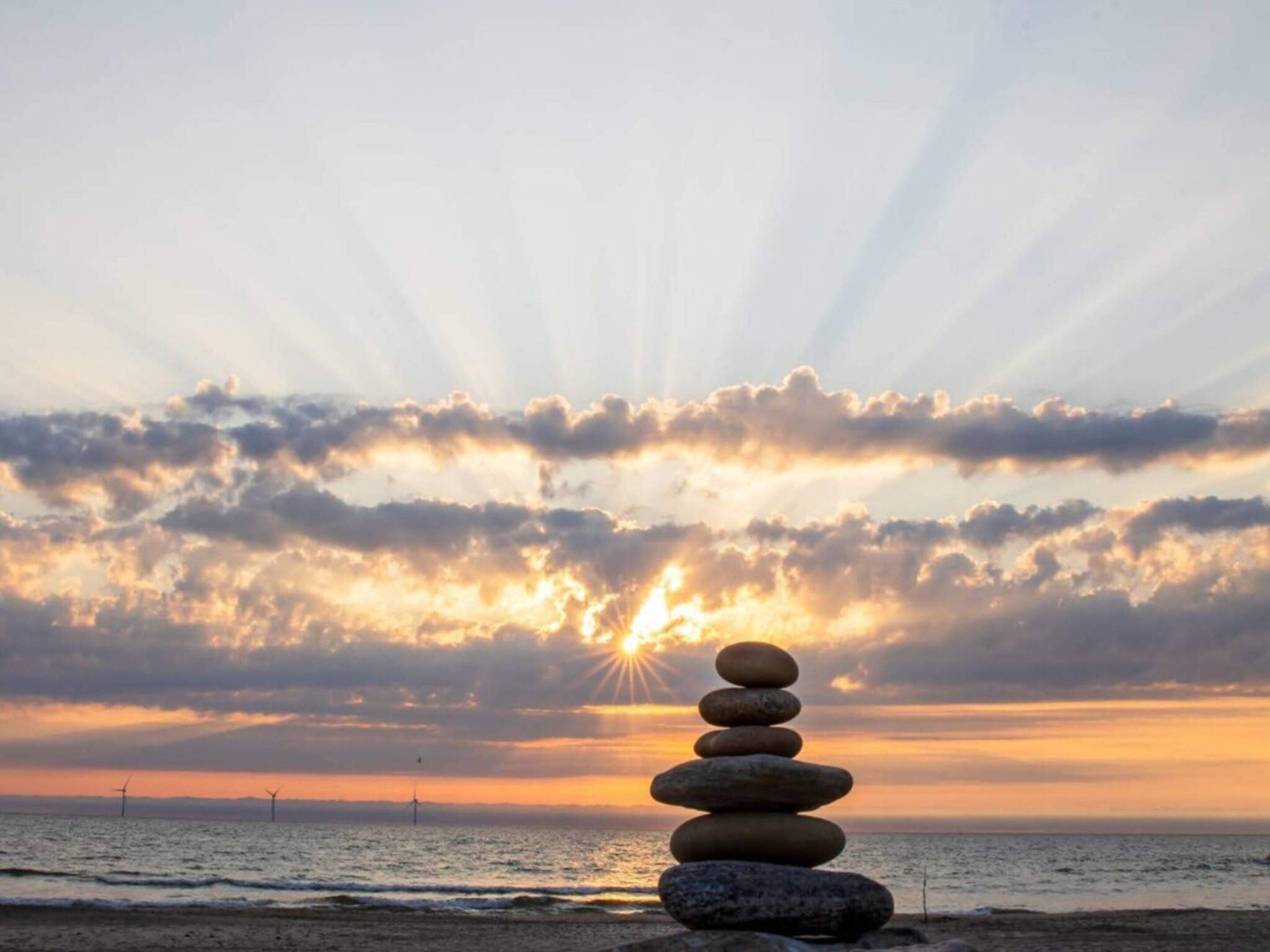 A stack of stones on a beach with the sun setting in the background.