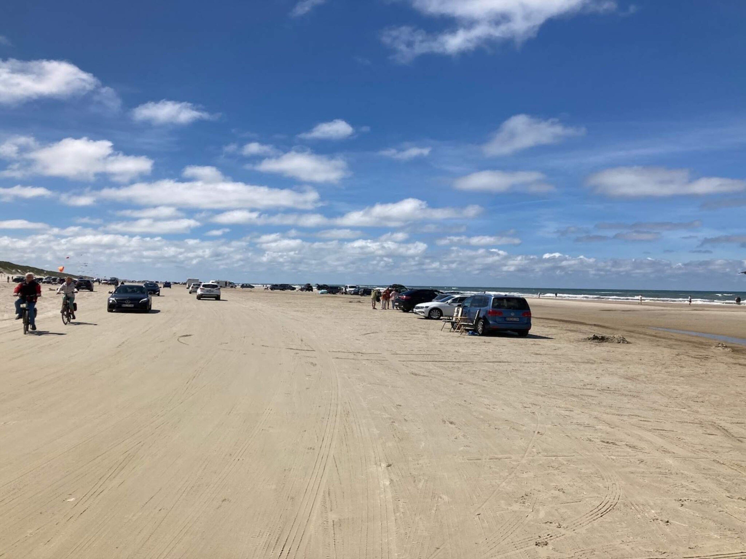 Een zandstrand met geparkeerde auto's en mensen die erover lopen.