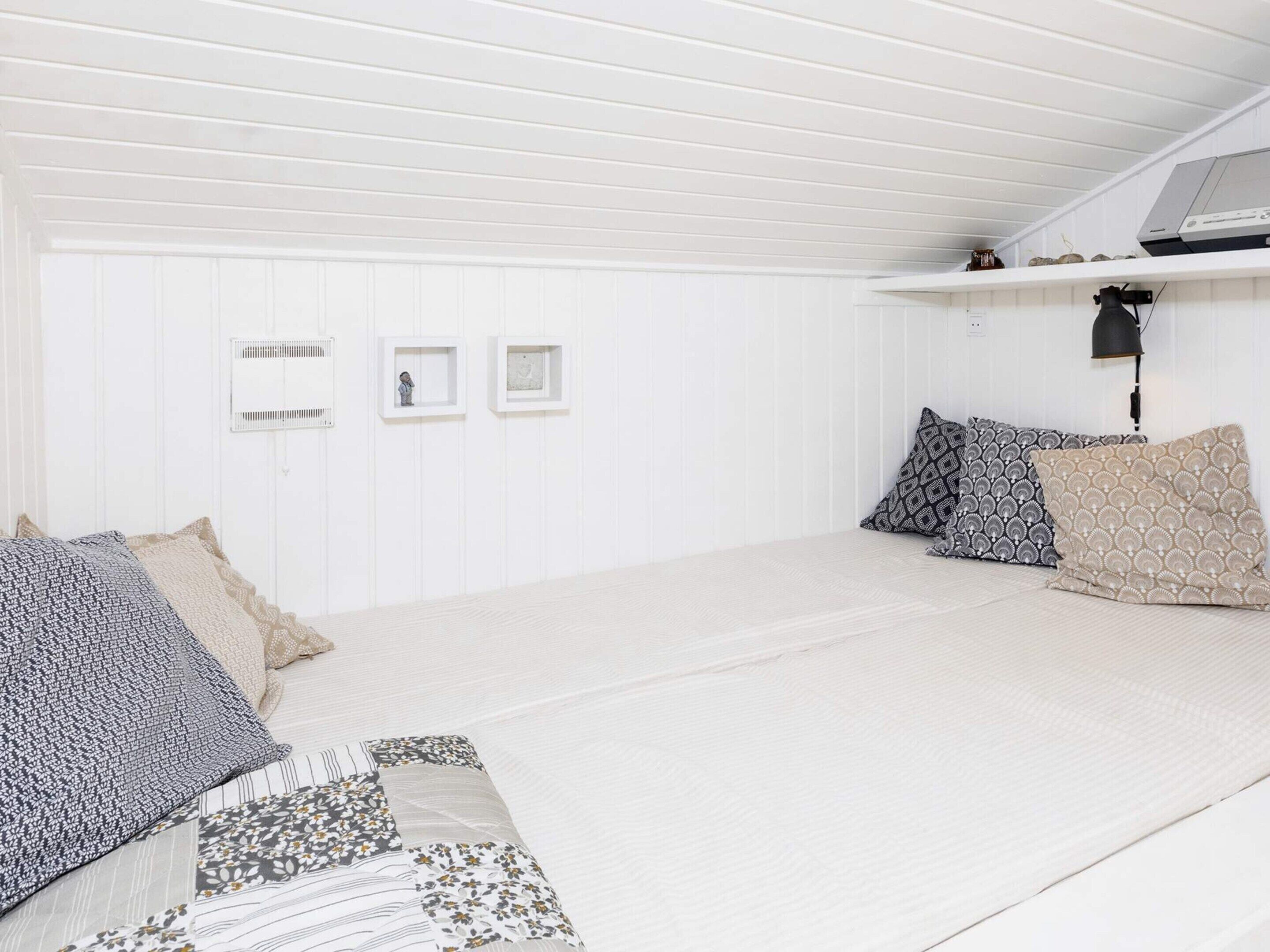 Ein Zimmer mit einem Bett, Kissen, einem Regal mit Dekoration und einer Wandleuchte.
