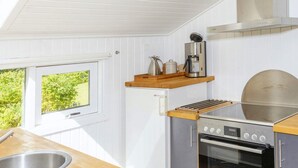 Une cuisine compacte équipée d’un four encastré, d’une machine à café et d’une fenêtre donnant sur un espace verdoyant.
