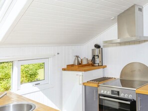 A compact kitchen with a built-in oven, a coffee maker, and a window with a view of greenery. - 6 Person Holiday Home in Fjerritslev (Fjerritslev)