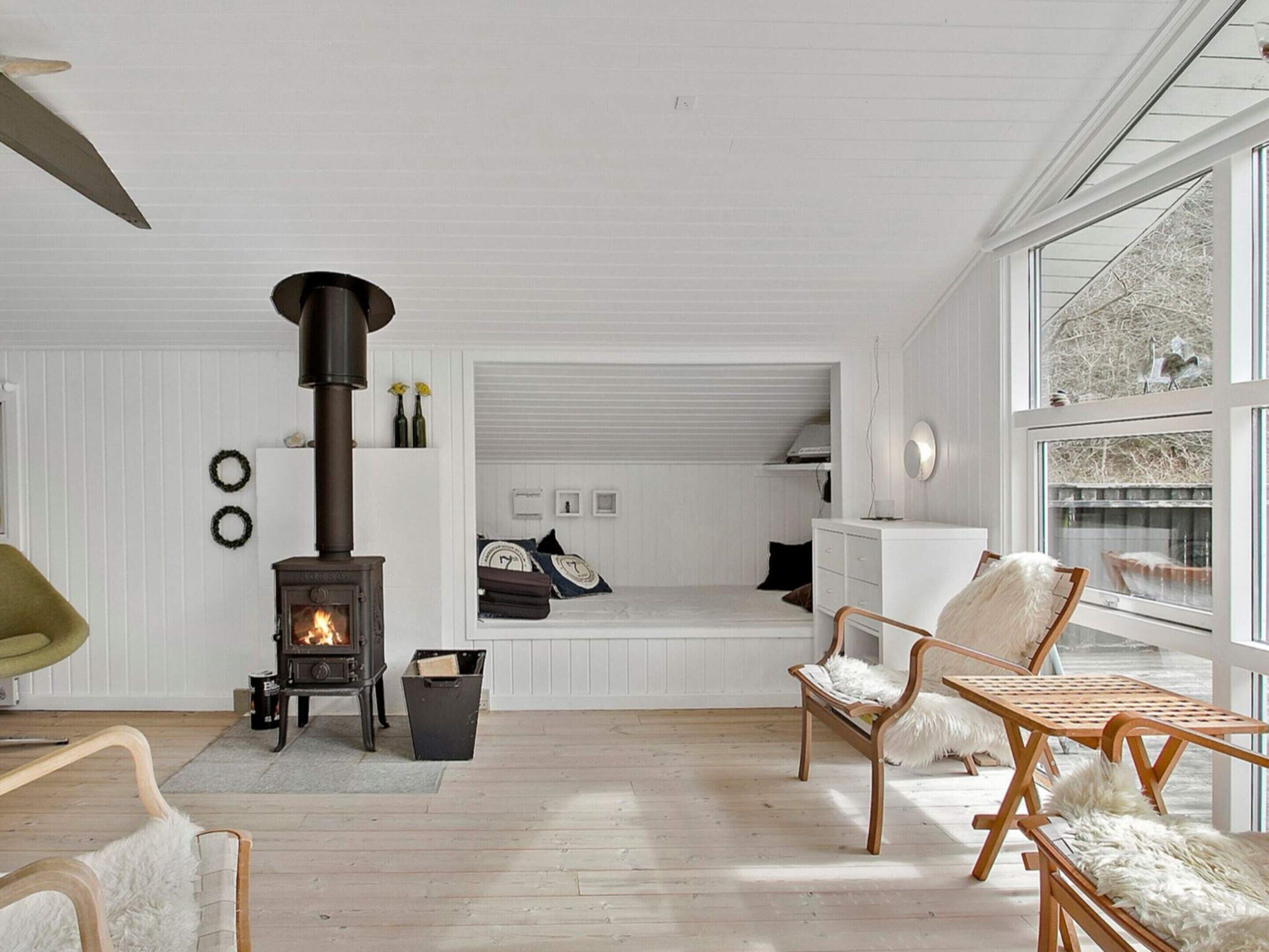 A cozy living room with a wood-burning stove, a dining area with a bench, and a view through large windows.
