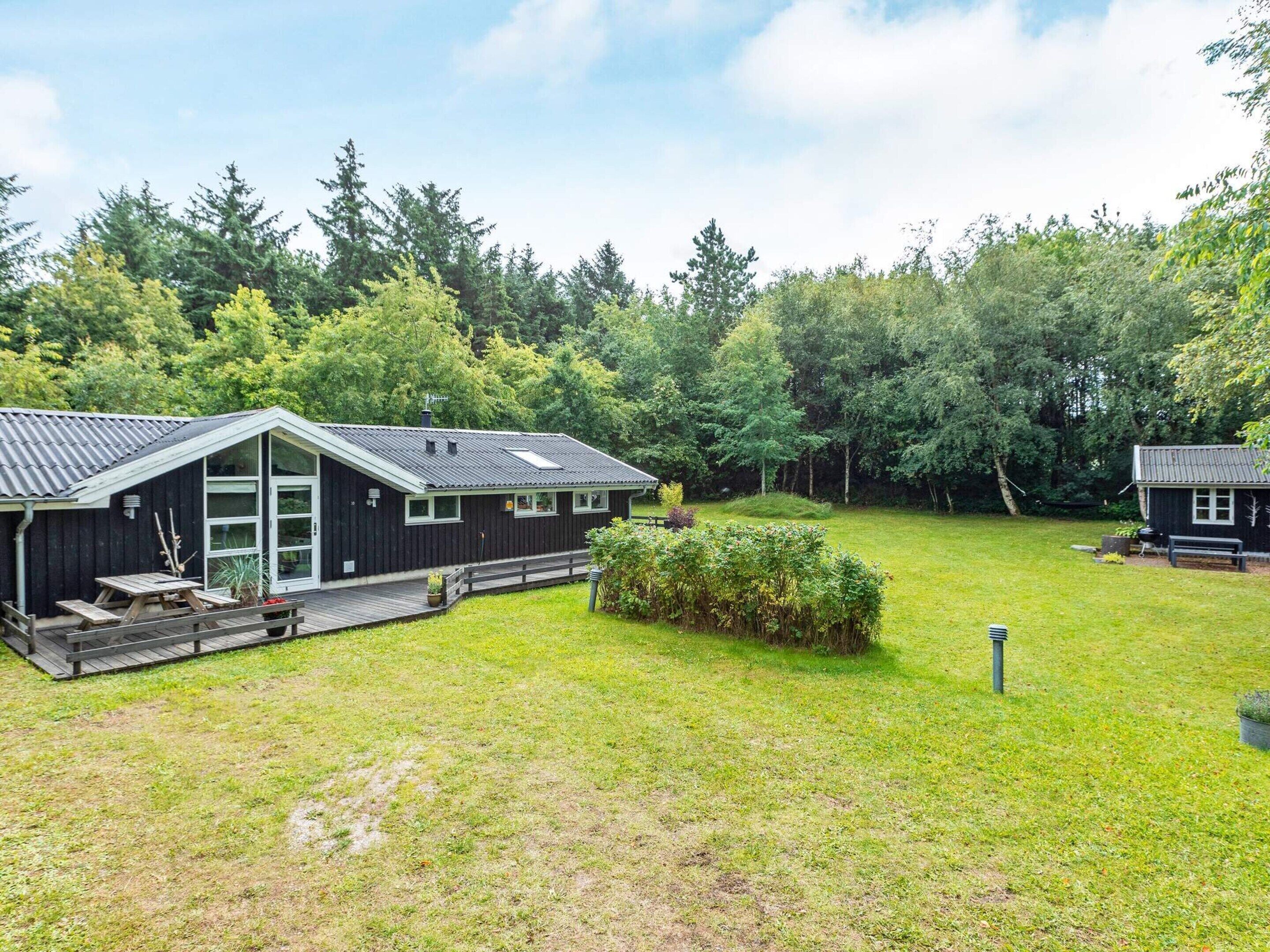 A cabin with a deck, surrounded by a grassy yard and dense forest.