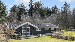 Une cabane dotée d’un toit en pente, de grandes fenêtres et d’une terrasse.