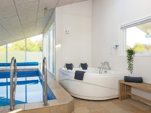 En moderne swimmingpool indendørs med jacuzzi, klare blå fliser og en træbænk.