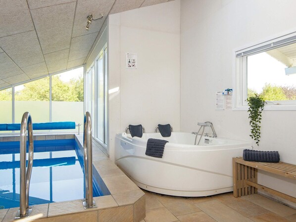 Une piscine intérieure moderne, dotée d’un jacuzzi, de carreaux bleus et d’un banc en bois.