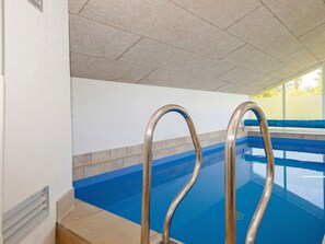 A swimming pool with metal handrails, tiled walls, and a clear view of the sky through the windows.