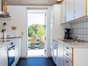 A kitchen with white cabinets, a coffee maker, and a view of greenery outside.