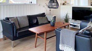 A modern living room with a black leather sofa, a wooden coffee table, and a television. - 10 Person Holiday Home in Juelsminde-by Traum (Horsens)