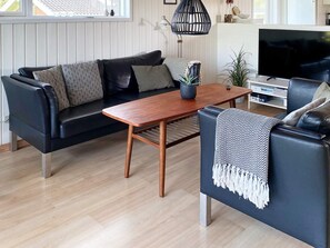 A modern living room with a black leather sofa, a wooden coffee table, and a television. - 10 Person Holiday Home in Juelsminde-by Traum (Horsens)