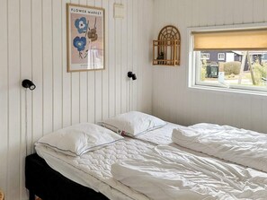 Une chambre à coucher avec un lit, des murs blancs, une fenêtre donnant sur un paysage agréable, un luminaire fixé au mur et une affiche.