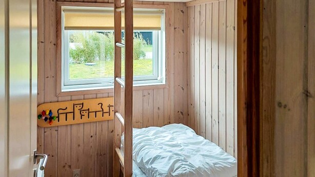 A wooden room with bunk beds, a window, and a wooden wall with a colorful decoration. - 10 Person Holiday Home in Juelsminde-by Traum (Horsens)