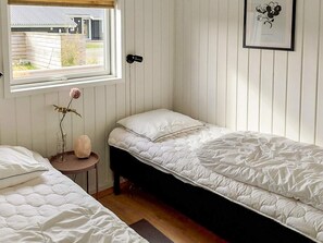 A bedroom with two beds, a window, a framed picture, and a small table with a vase.