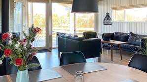 A modern living room with a dining area, featuring a sofa, a table with a vase of flowers, and a pendant light. - 10 Person Holiday Home in Juelsminde-by Traum (Horsens)